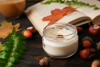 Burning candle, book and autumn leaves on wooden table