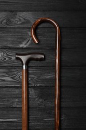 Different elegant walking canes on black wooden table, flat lay