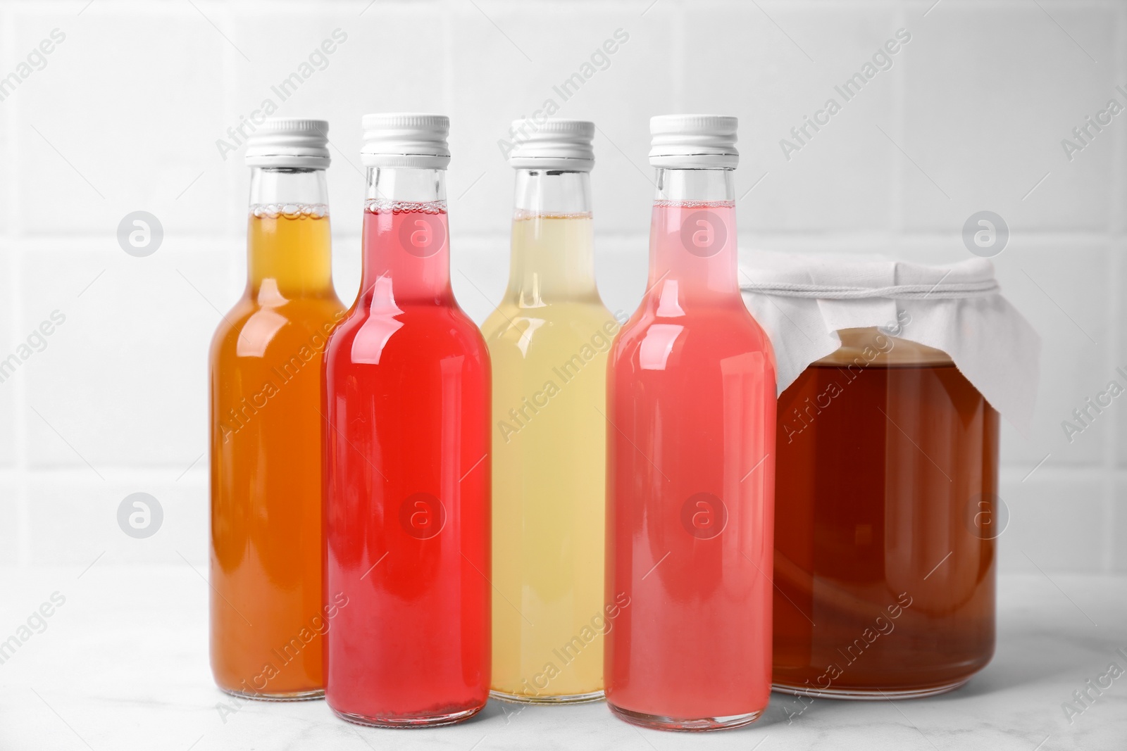 Photo of Delicious kombucha in glass bottles and jar on white marble table