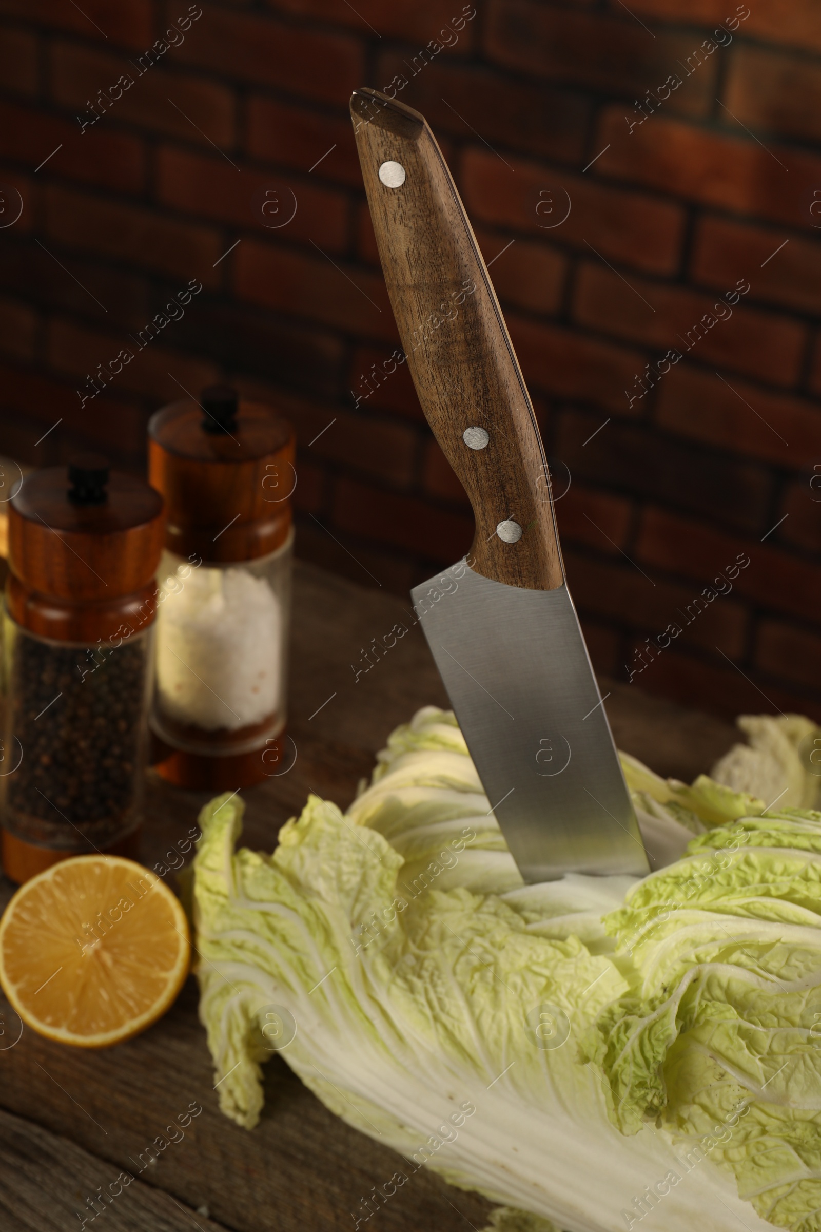 Photo of Fresh Chinese cabbage, knife, spices and lemon on wooden table