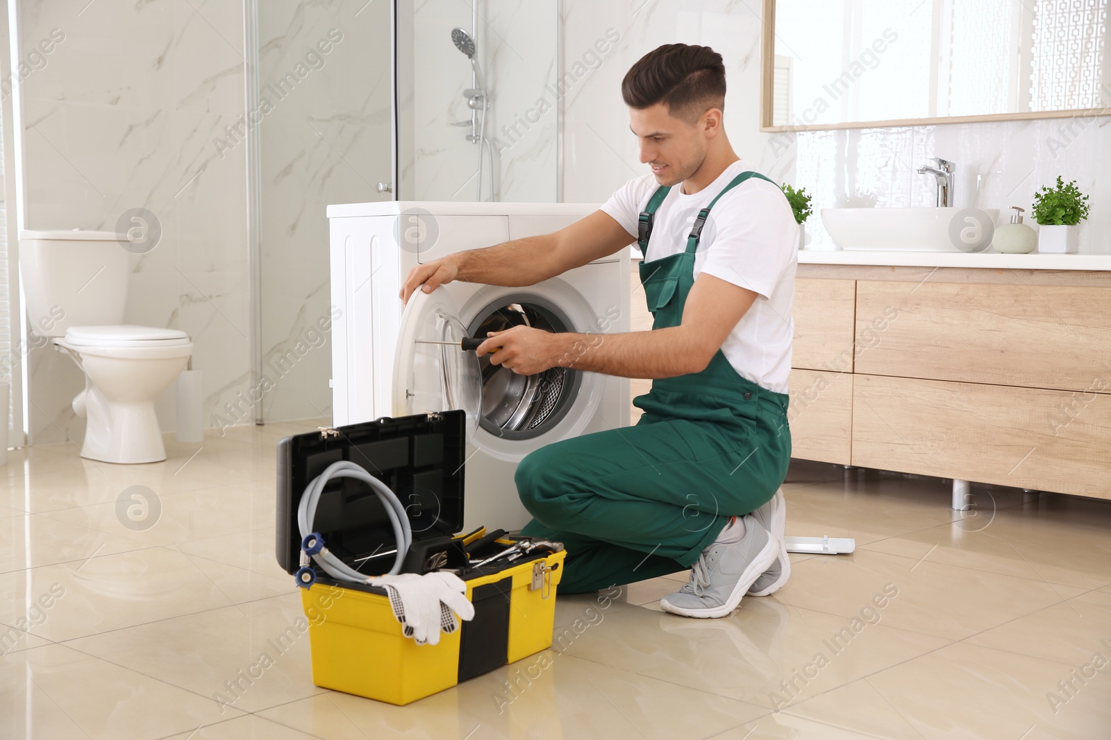 Photo of Professional plumber repairing washing machine in bathroom