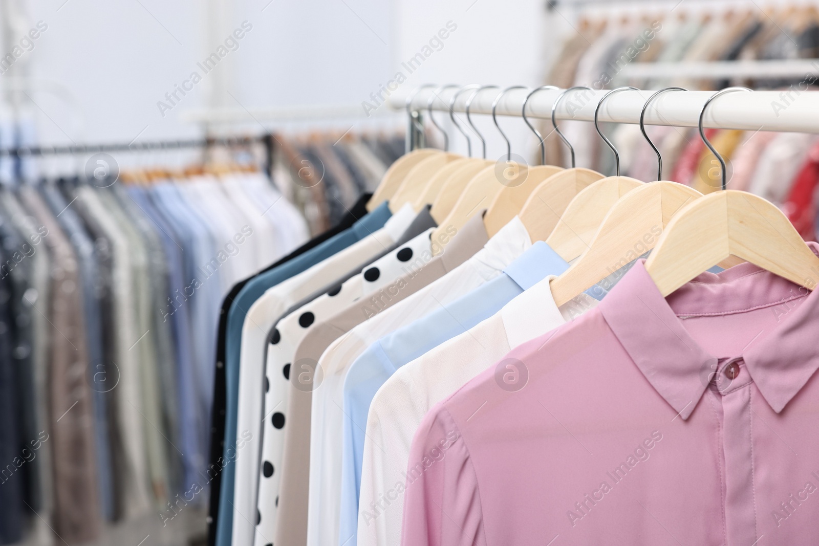 Photo of Dry-cleaning service. Many different clothes hanging on rack indoors, closeup