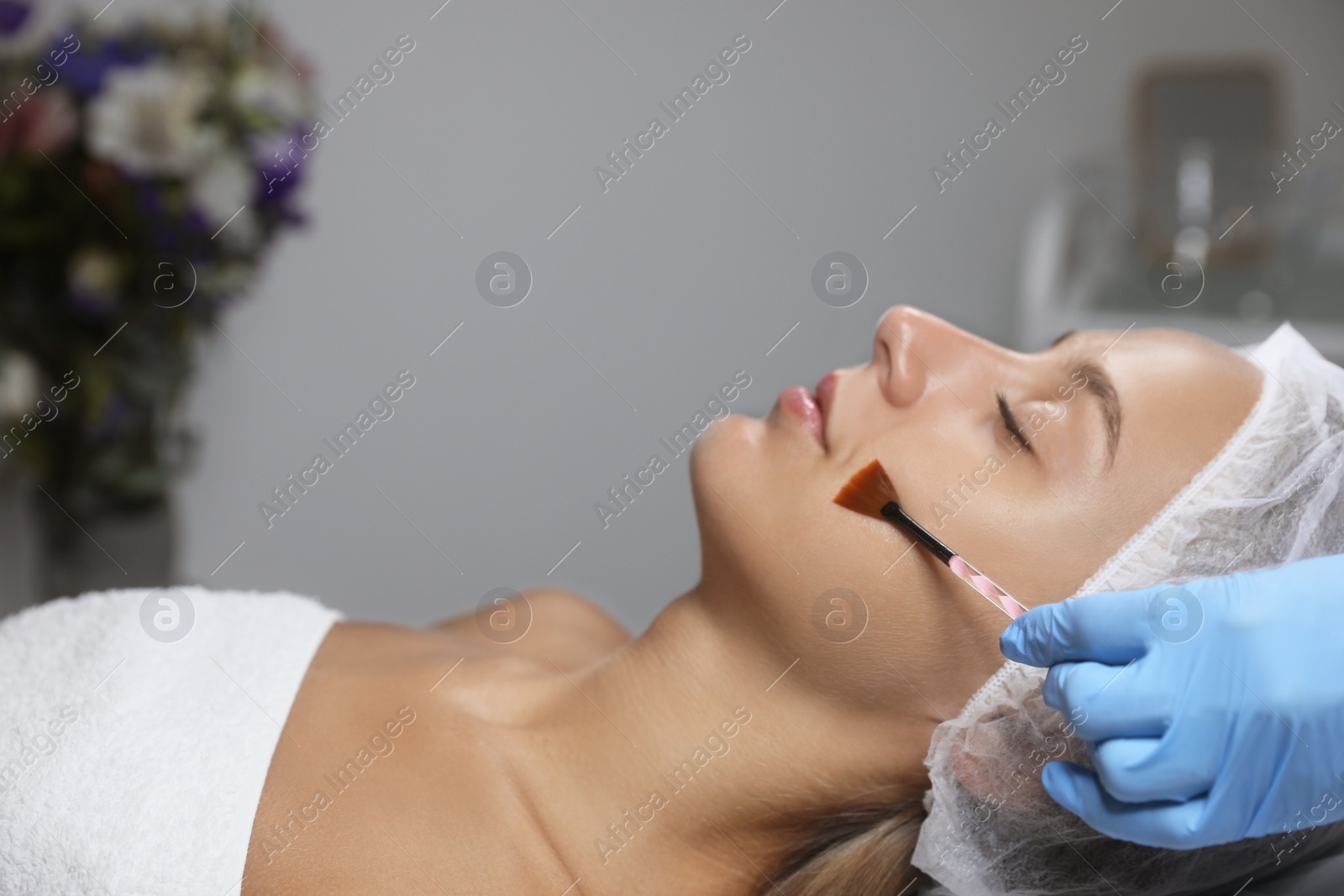 Photo of Cosmetologist applying chemical peel product on client's face in salon