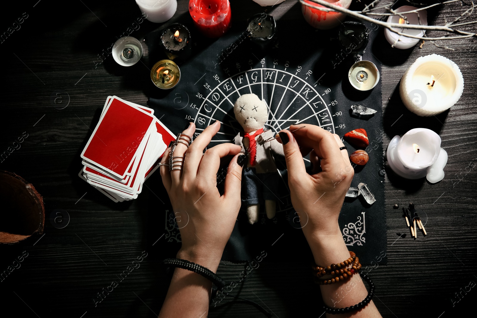 Photo of Woman stabbing voodoo doll with needle at table, closeup. Curse ceremony