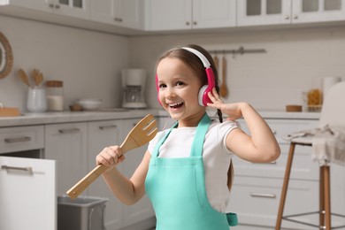 Photo of Cute little girl with headphones and fork spatula singing in kitchen