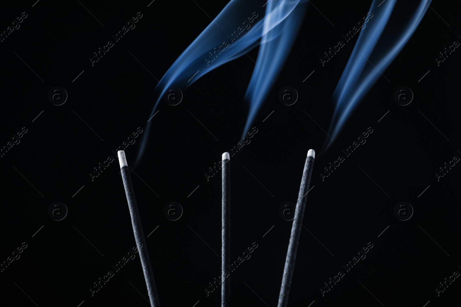 Photo of Incense sticks smoldering on black background, closeup