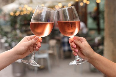 Photo of Women clinking glasses with rose wine outdoors, closeup