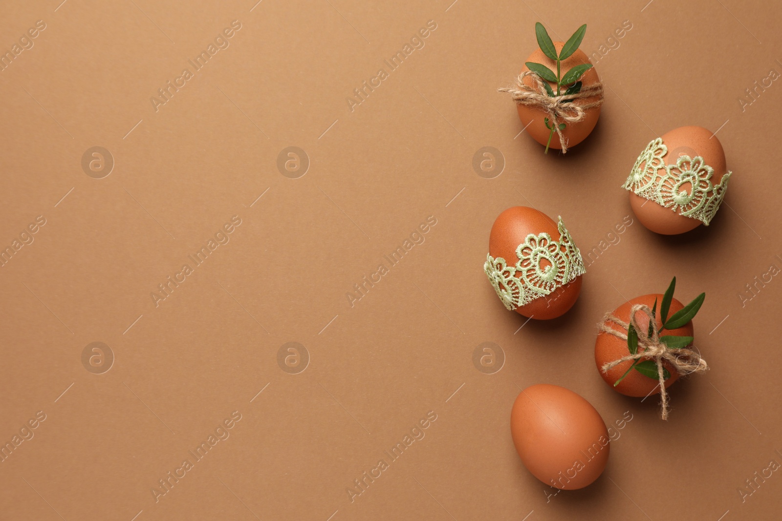 Photo of Festively decorated chicken eggs on brown background, flat lay and space for text. Happy Easter