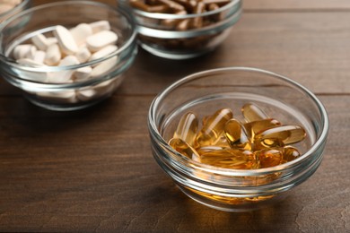 Photo of Different dietary supplements in glass bowls on wooden table, closeup