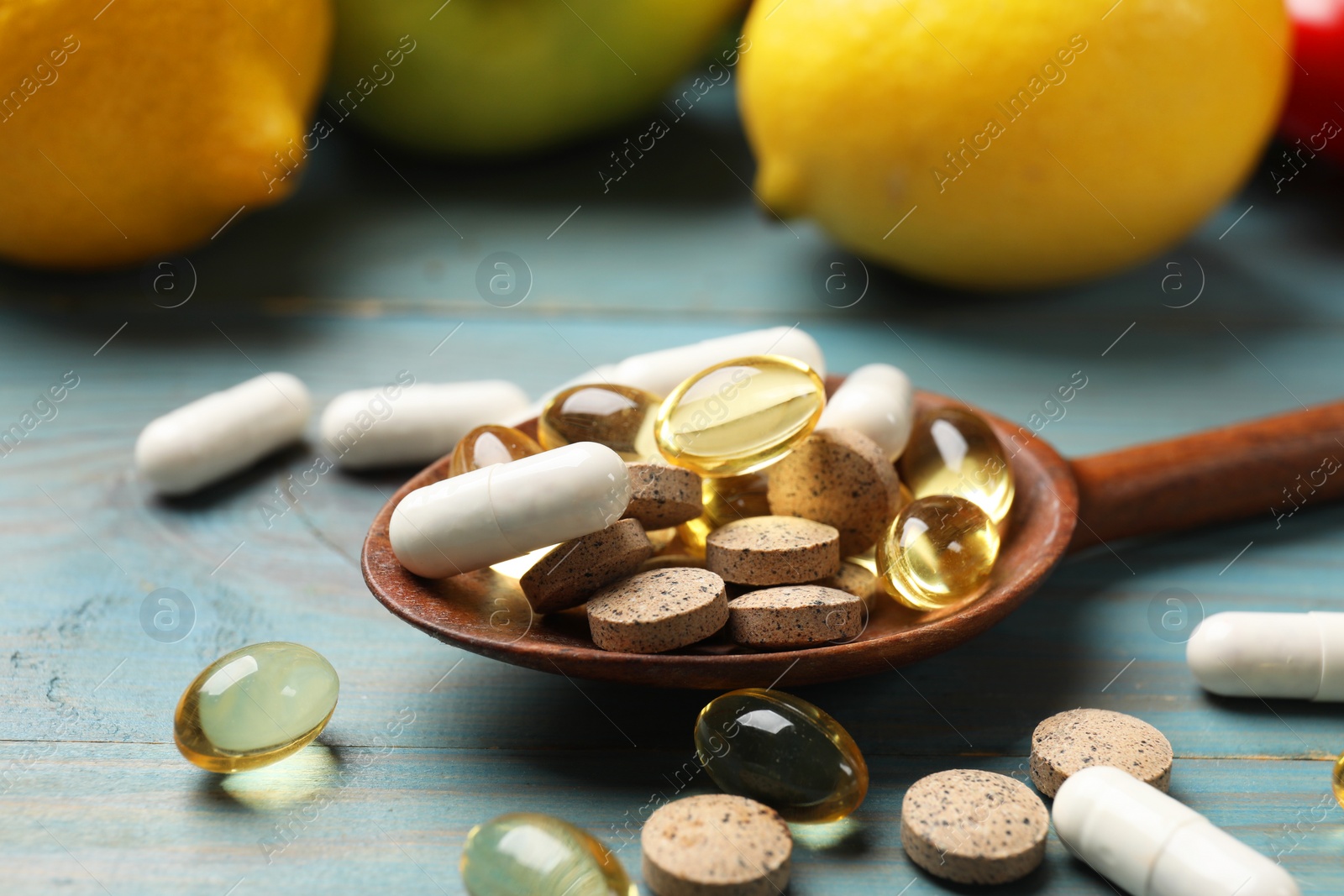 Photo of Dietary supplements. Spoon with different pills near food products on light blue wooden table, closeup