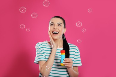 Photo of Young woman having fun with soap bubbles on pink background