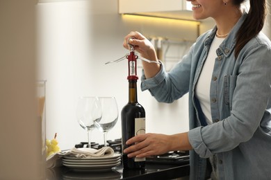 Photo of Smiling woman opening wine bottle with corkscrew at countertop indoors, closeup