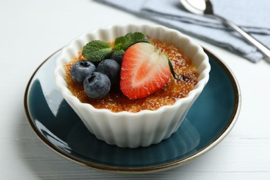Photo of Delicious creme brulee with berries and mint in bowl on white wooden table, closeup