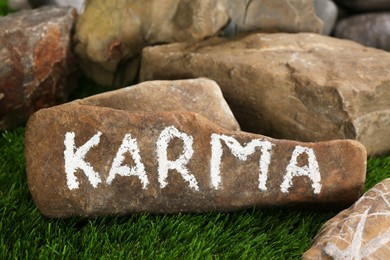 Photo of Stone with word Karma on green grass, closeup