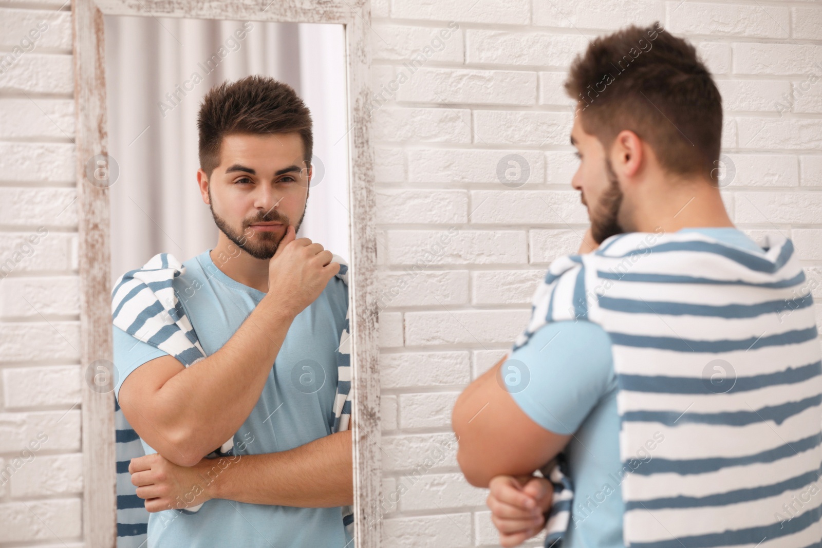 Photo of Young man looking at himself in large mirror at home