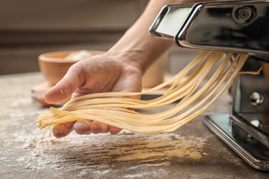 Woman preparing noodles with pasta machine at table
