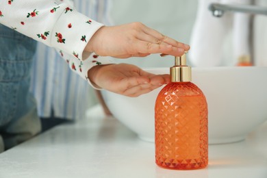 Photo of Little girl washing hands with liquid soap in bathroom, closeup