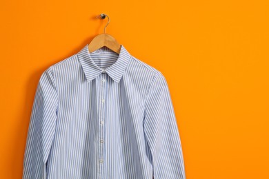 Hanger with striped shirt on orange wall, space for text