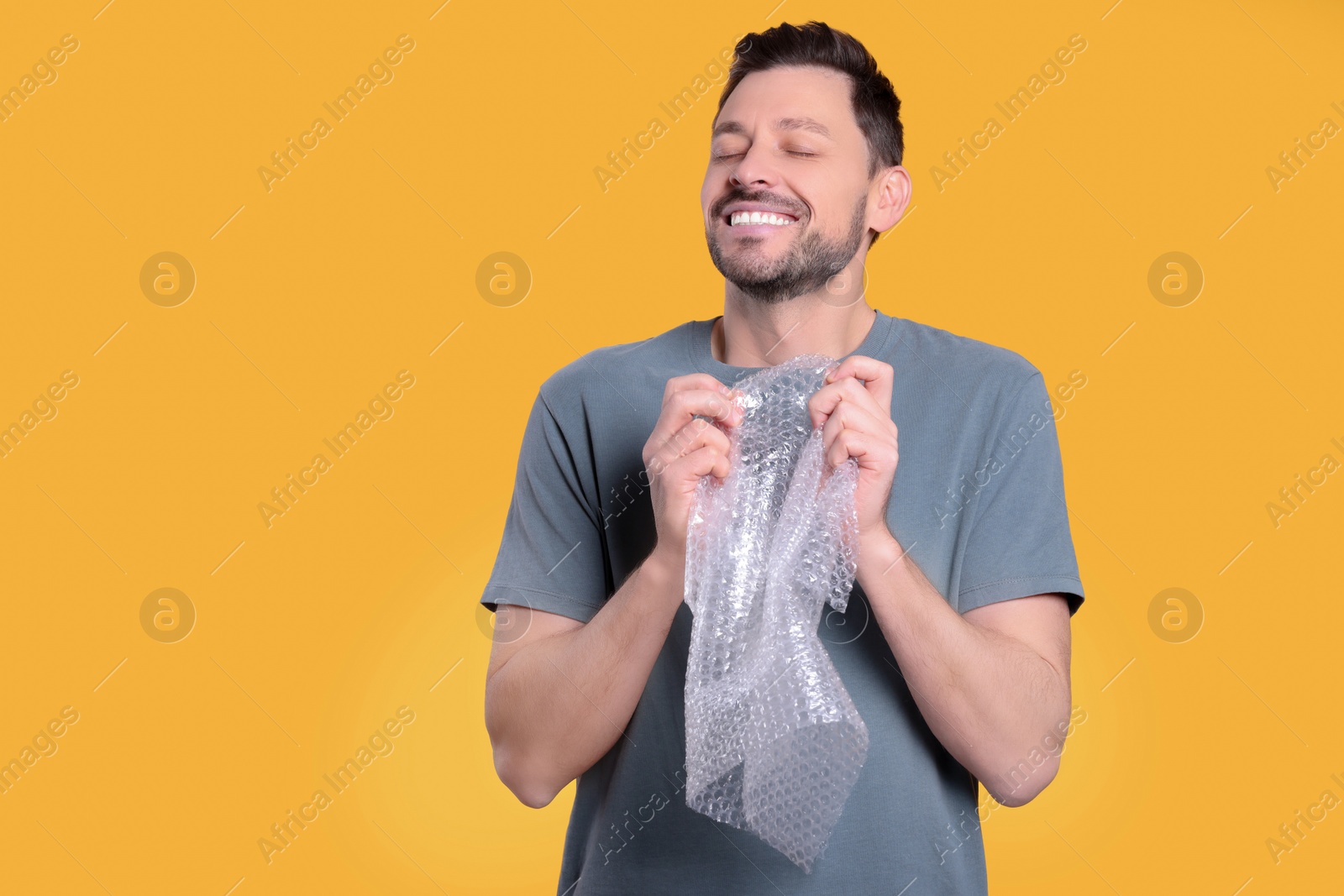 Photo of Man popping bubble wrap on yellow background, space for text. Stress relief