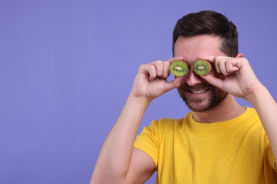 Photo of Man covering his eyes with halves of kiwi on purple background. Space for text