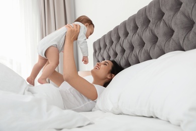 Young mother playing with her cute baby on bed indoors