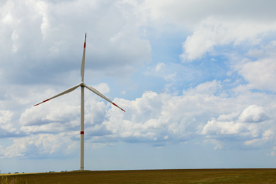 Photo of Modern wind turbine in field on cloudy day. Alternative energy source