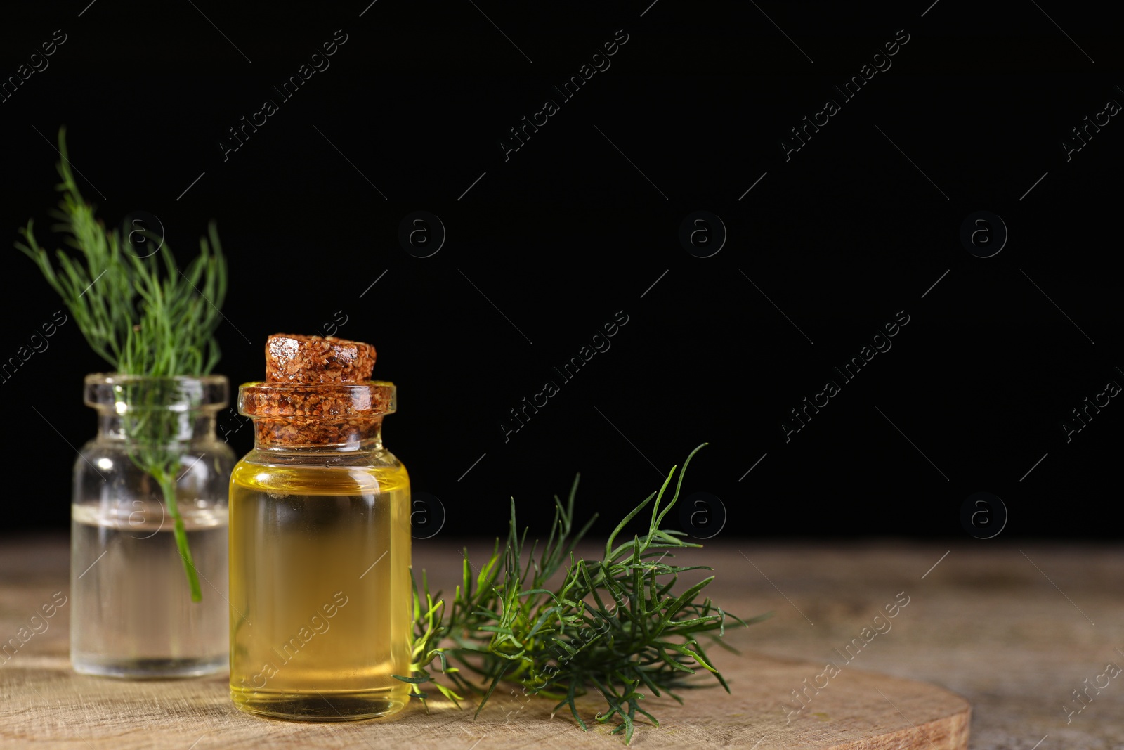 Photo of Bottles of essential oil and fresh dill on wooden table against black background. Space for text