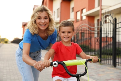 Photo of Happy mother teaching her son to ride bicycle in city