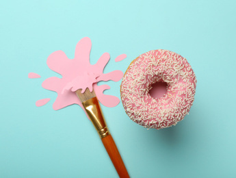 Photo of Artist's brush with paint blot and donut on light blue background, flat lay