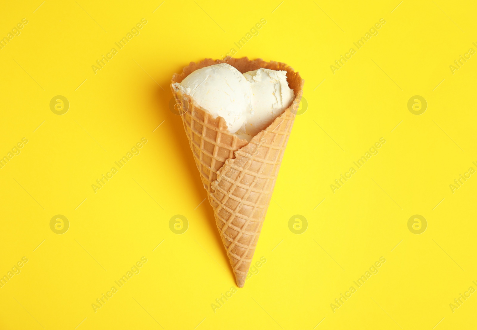 Photo of Delicious vanilla ice cream in wafer cone on yellow background, top view