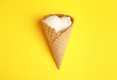 Delicious vanilla ice cream in wafer cone on yellow background, top view