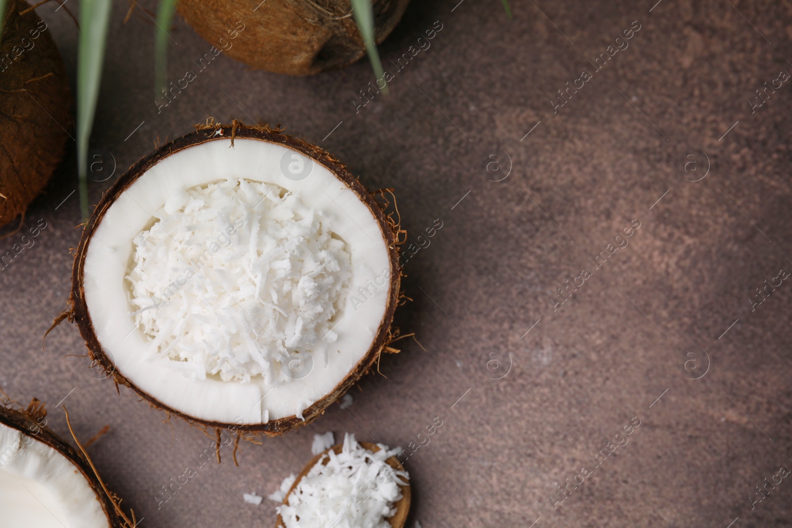 Photo of Coconut flakes in nut shell and spoon on brown table, flat lay. Space for text