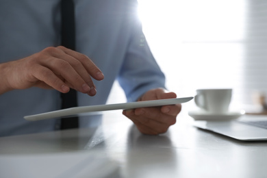 Photo of Businessman working with modern tablet at white table in office, closeup