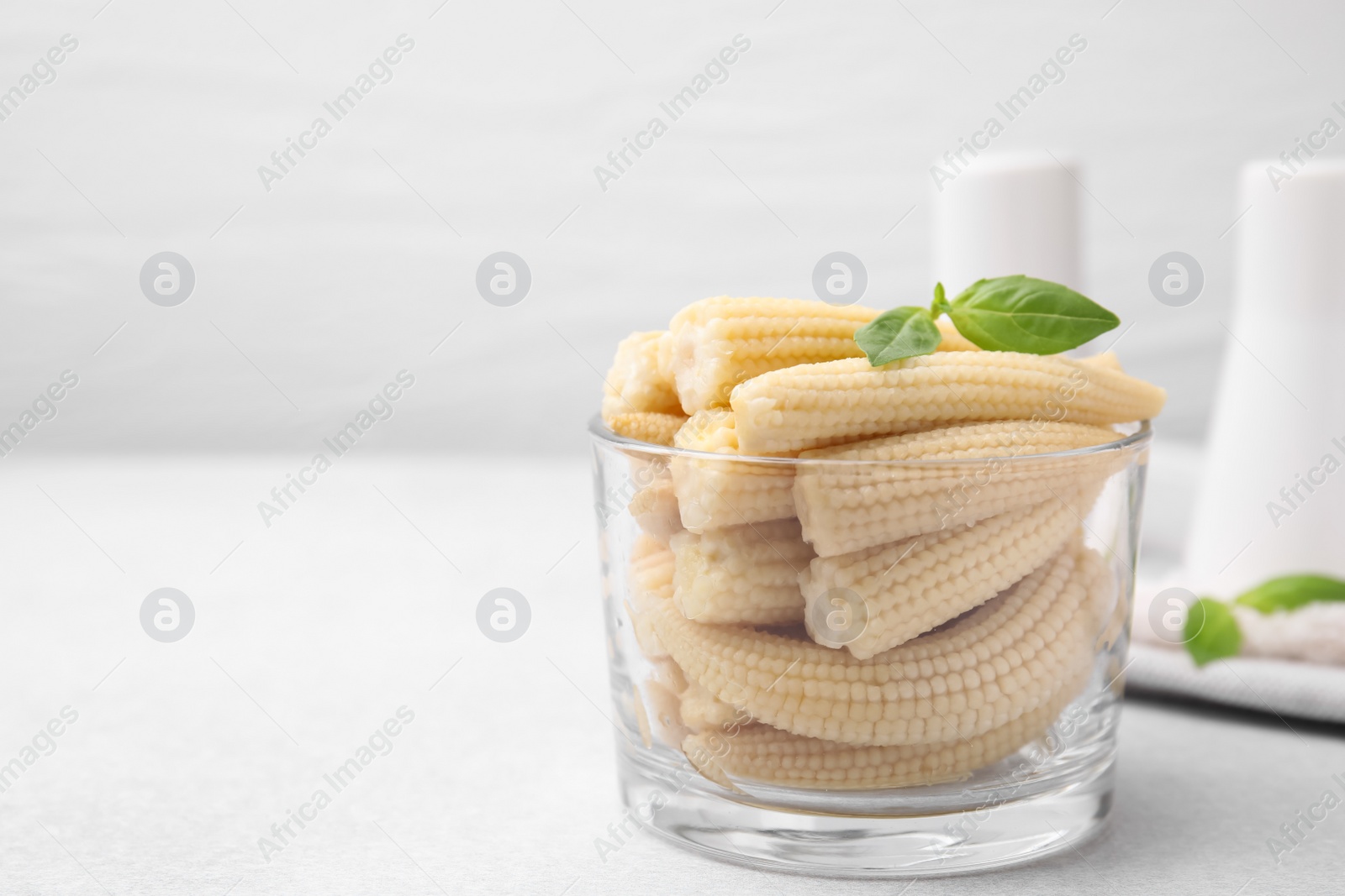 Photo of Canned baby corns with basil on white table, closeup. Space for text