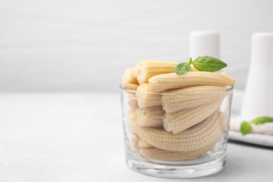 Canned baby corns with basil on white table, closeup. Space for text