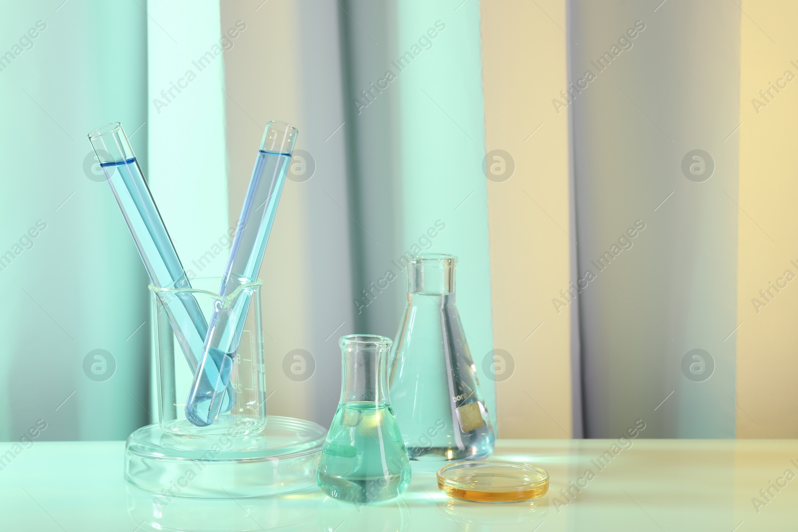 Photo of Laboratory analysis. Different glassware on table against color background, space for text