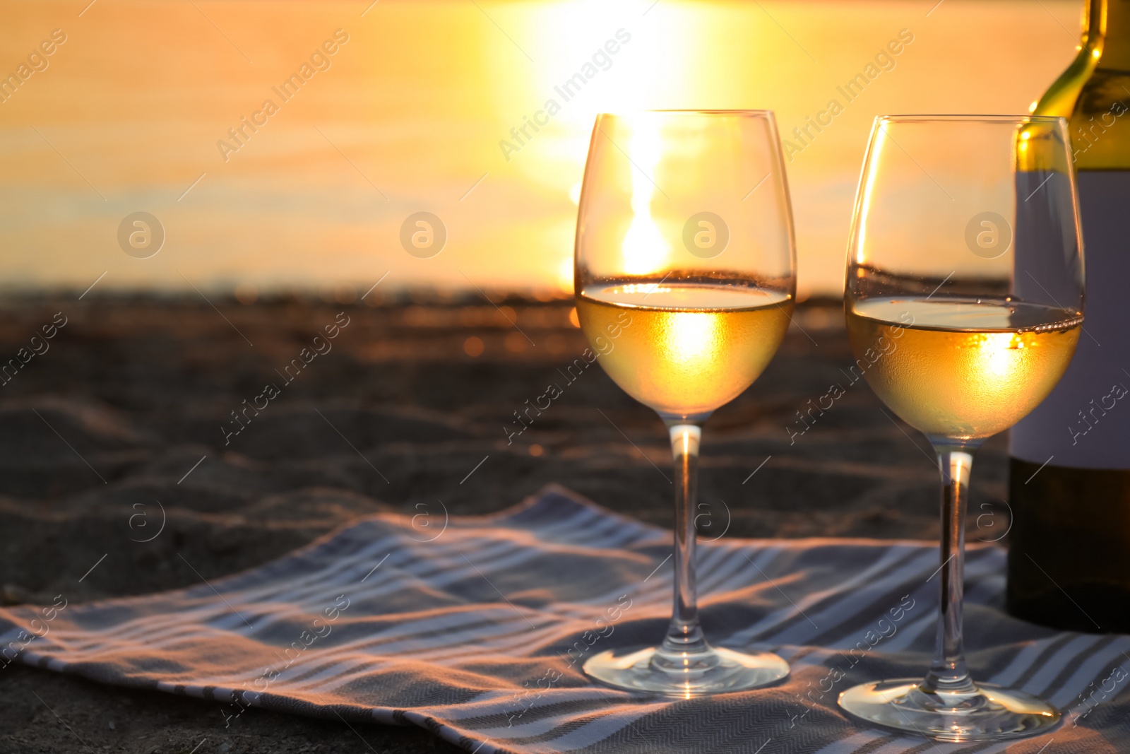 Photo of Bottle and glasses of delicious wine on riverside at sunset