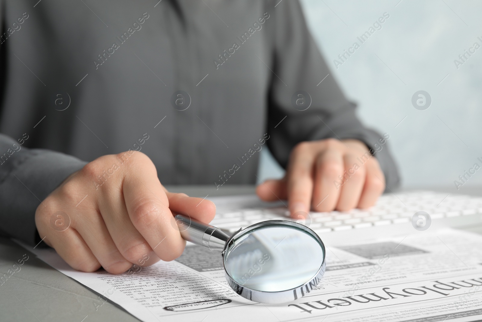 Photo of Woman looking through magnifying glass at newspaper, closeup. Job search concept