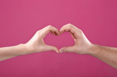 Photo of Man and woman making heart with their hands on color background, closeup