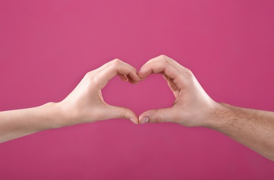 Man and woman making heart with their hands on color background, closeup