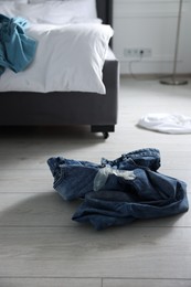 Photo of Unrolled condom and jeans on floor in bedroom. Safe sex