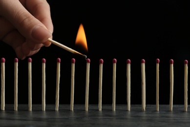Photo of Woman igniting line of matches on table against black background, closeup