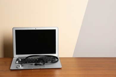 Modern laptop with stethoscope on table against color wall. Mockup for design