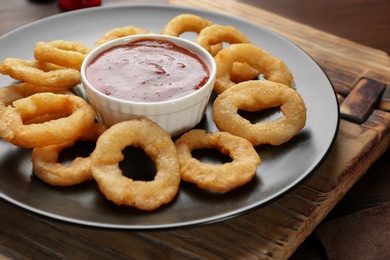 Photo of Plate with fried onion rings and sauce on table