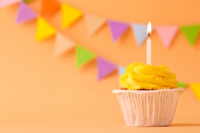 Photo of Tasty birthday cupcake with candle on orange table against party flags. Space for text