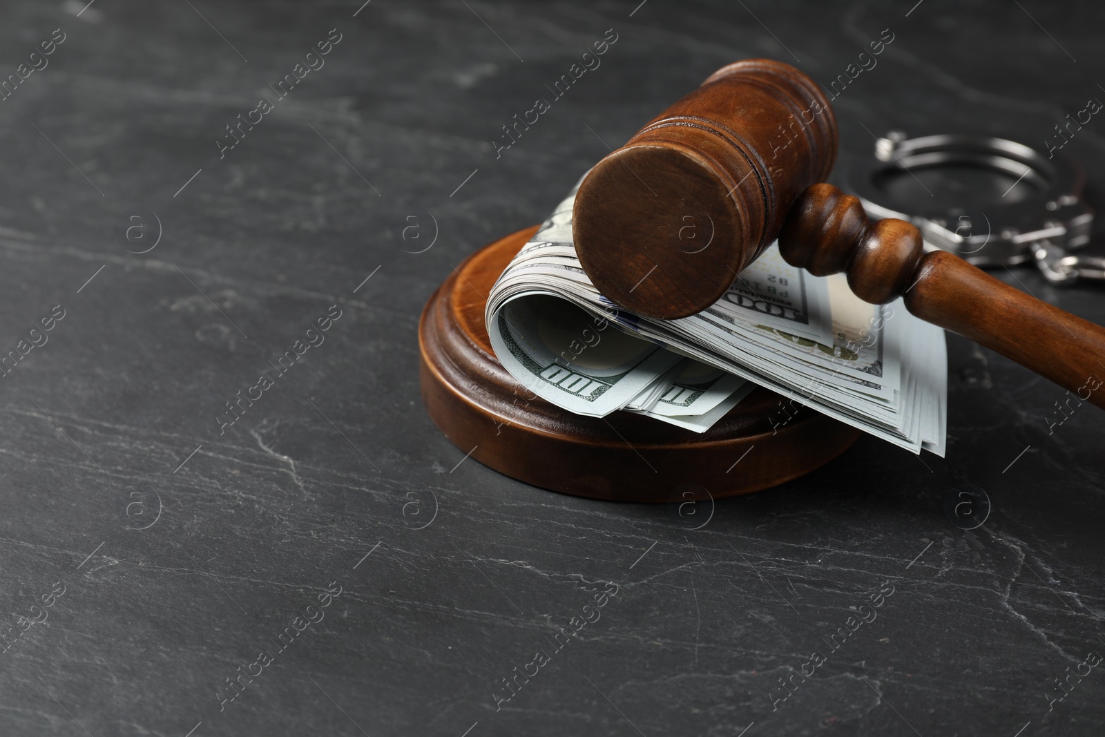 Photo of Judge's gavel, money and handcuffs on dark grey table. Space for text