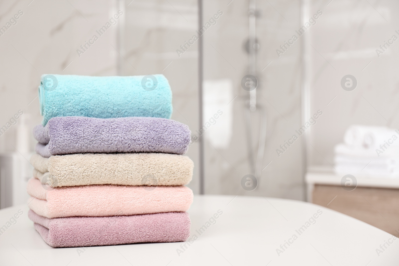 Photo of Stack of color towels on white table in bathroom. Space for text