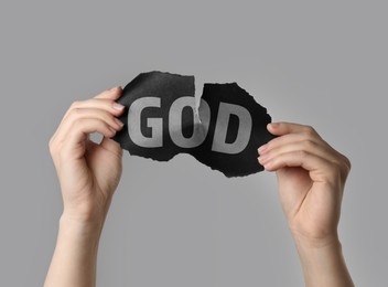 Image of Atheism as religious position. Woman ripping black paper with word God on light grey background, closeup