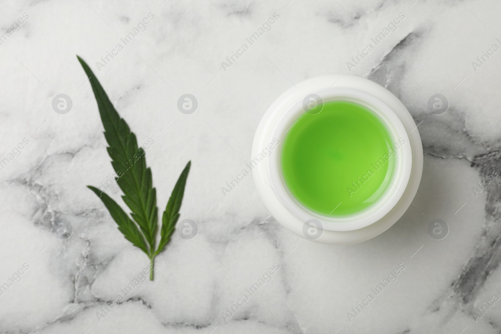 Photo of Jar of hemp cosmetics and green leaf on white marble table, flat lay