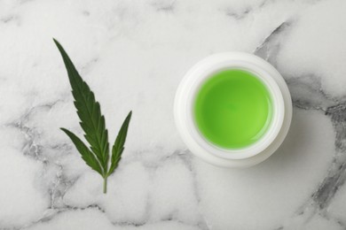 Photo of Jar of hemp cosmetics and green leaf on white marble table, flat lay